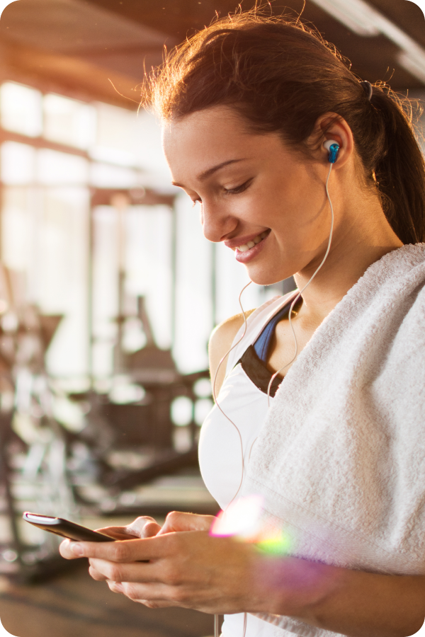 Woman at gym with towel and headphones.